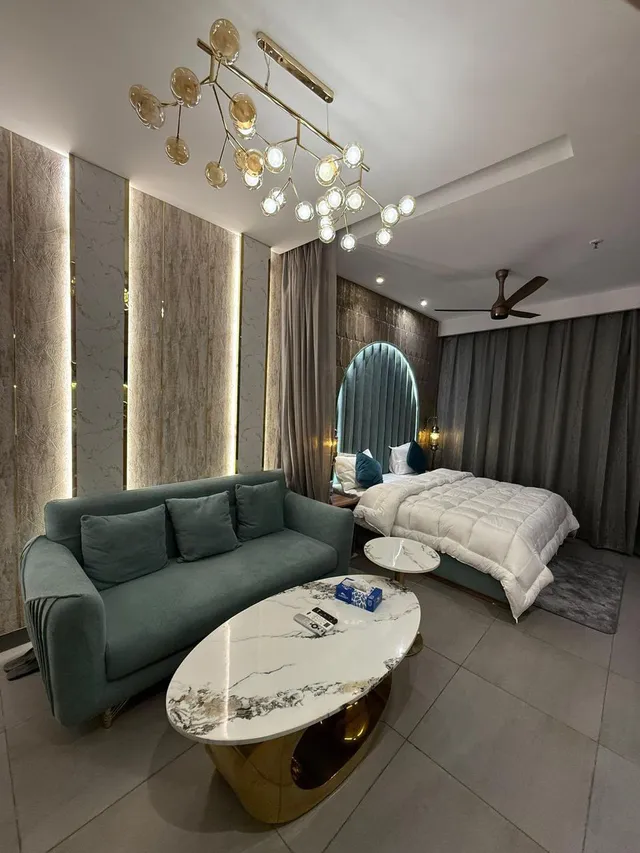 Bedroom seating with a green sofa, a curved headboard and illuminated wall panels.
