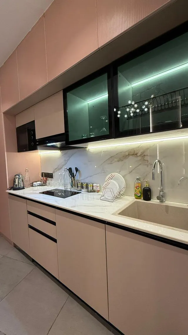 Blush-coloured kitchen cabinetry, glazed upper cupboards and a lit worktop.