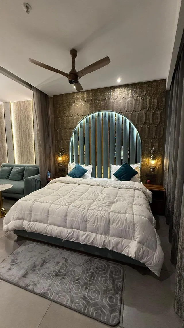 A curved green headboard, upholstered bed and patterned feature wall.