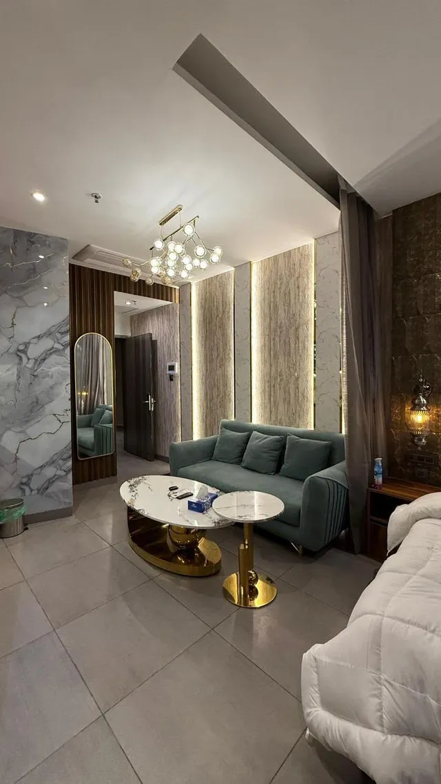 Green upholstered seating, nesting tables and vertical lighting beside a bedroom.