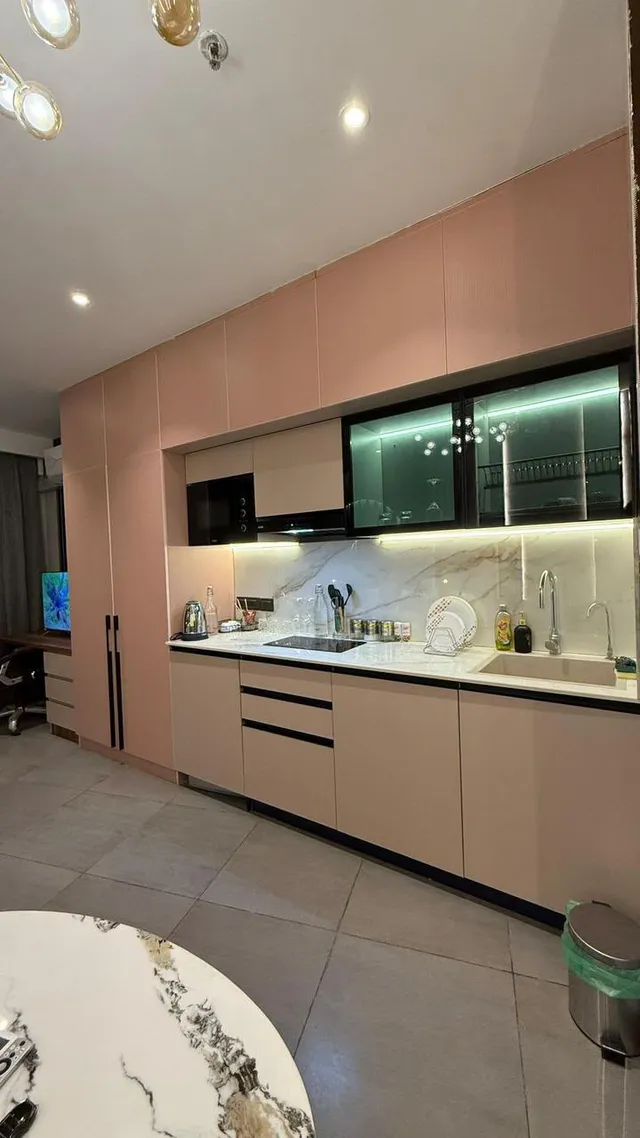 A wider view of blush kitchen cabinets and the continuous illuminated counter.