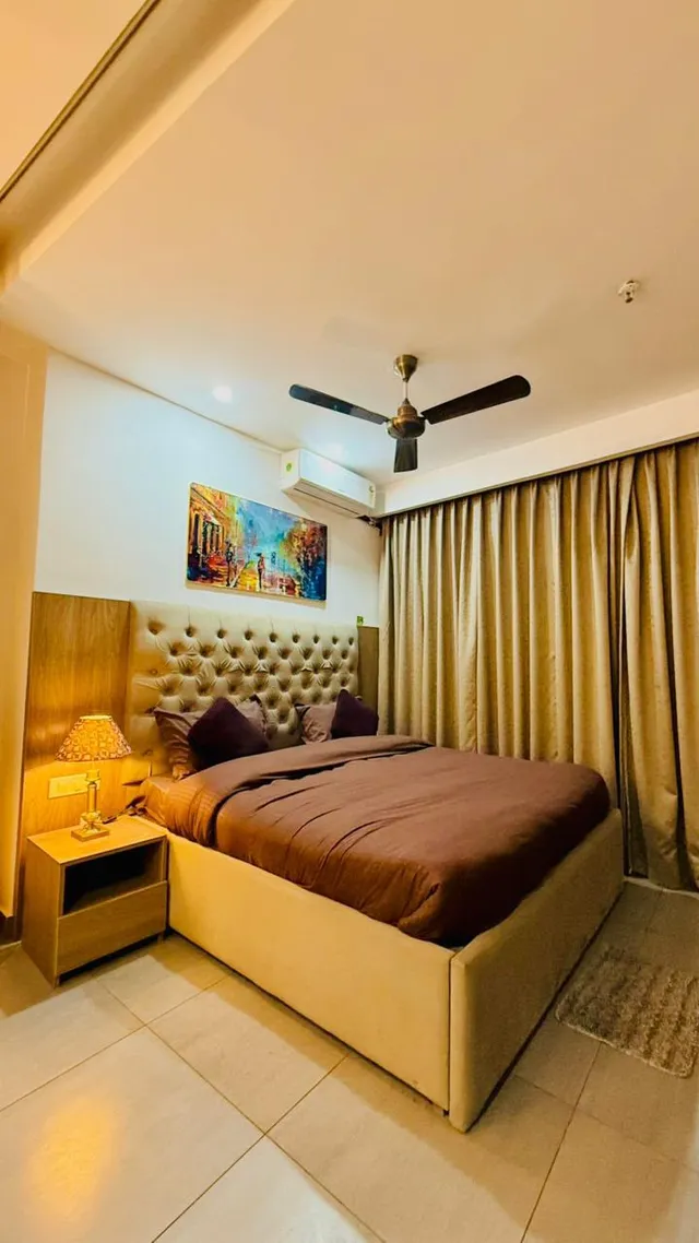 An upholstered bed, bedside lighting and full-height curtains in a warm bedroom.